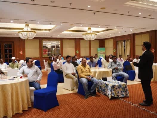 Aadesh Sharma leading a training session, with participants seated at round tables in a hotel ballroom